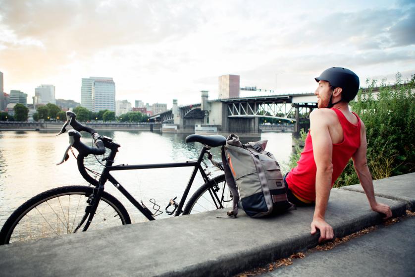 Male bike commuter sitting along the waterfront at sunset