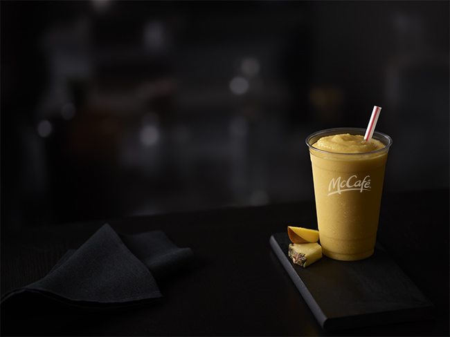 McCaf? Mango Pineapple Smoothie in Plastic Cup with Straw, Dark, Wood Table Surface, Dark, Indoor Background